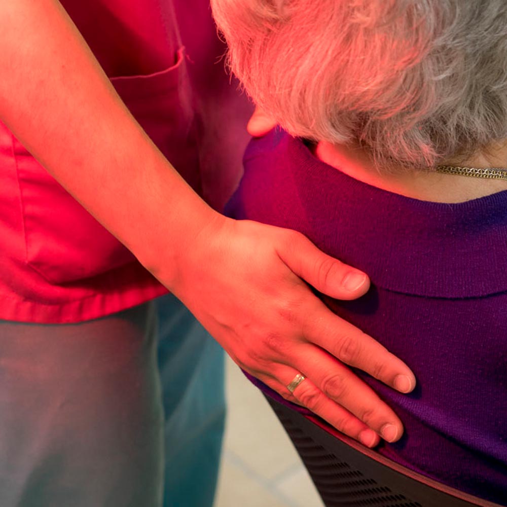 Una trabajadora coloca su mano en la espalda de una residentes mientras está sentada